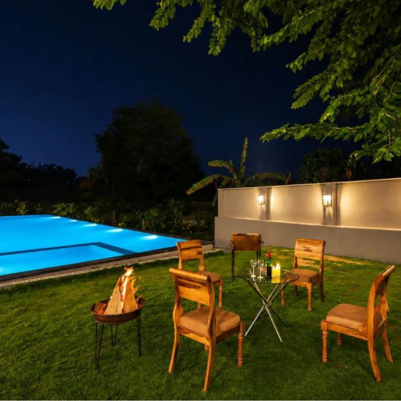 Evening Bonfire and Seating at Villa Miraan – Large Group Villa with Pool Udaipur Outdoor seating arrangement and lit bonfire on a grassy lawn next to a pool at a large group villa with pool Udaipur.