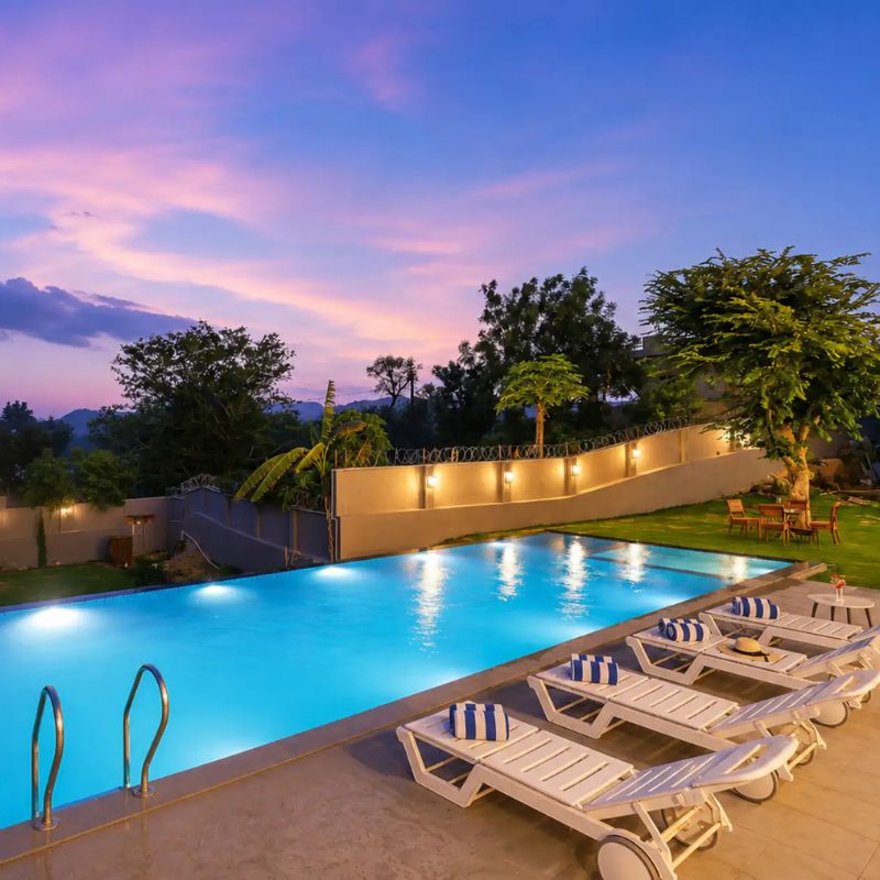 Illuminated Private Pool at Villa Miraan – 9 BHK Villa Udaipur Large illuminated outdoor swimming pool with white lounge chairs at a 9 BHK villa Udaipur at twilight.