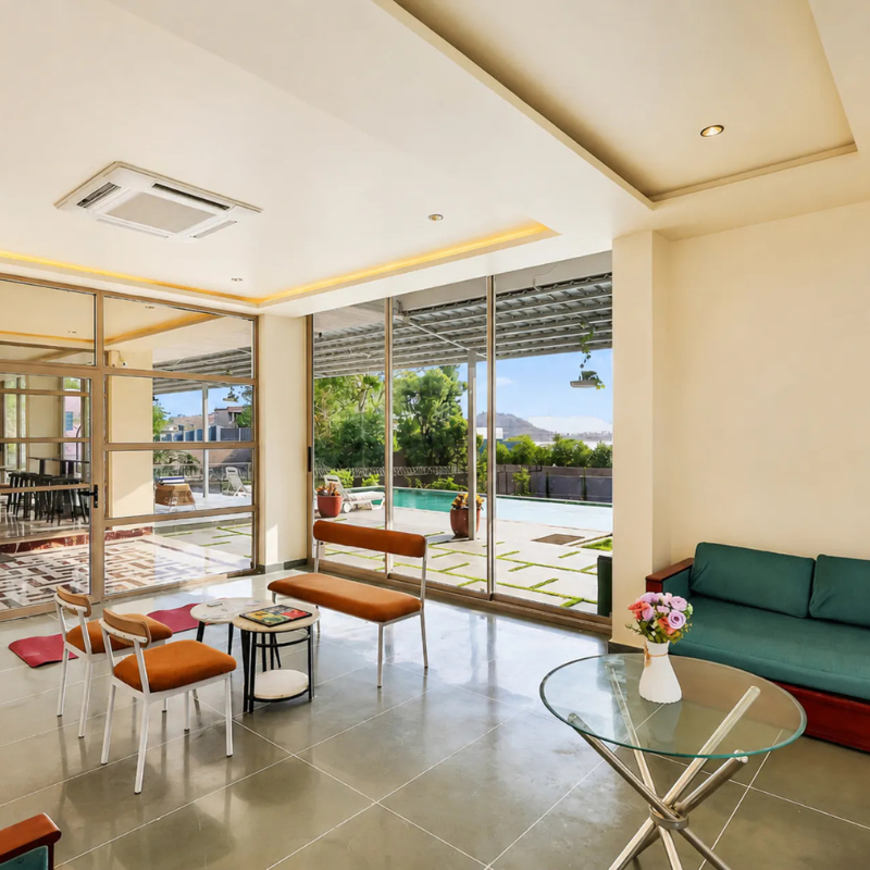 Indoor Lounge Area at Villa Miraan – 9 BHK Villa Udaipur Bright indoor lounge area with modern seating looking out to the pool at a 9 BHK villa Udaipur.