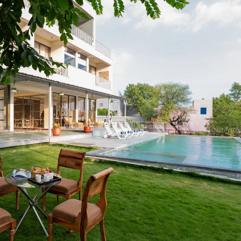 Lush Lawn and Exterior at Villa Miraan – Large Group Villa with Pool Udaipur Beautiful green lawn with a tea table setup next to the swimming pool at a large group villa with pool Udaipur.