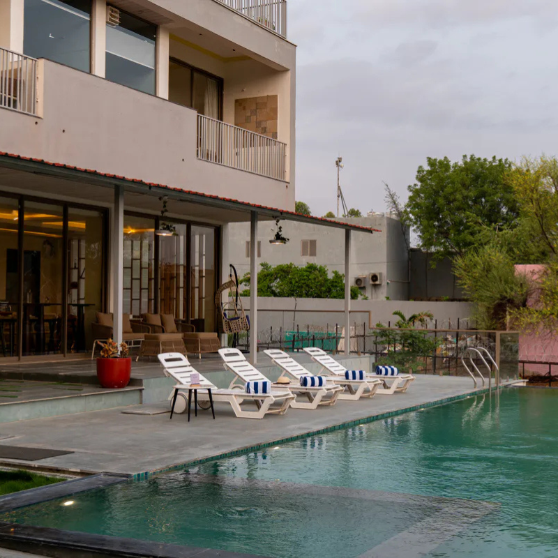 Poolside Deck at Villa Miraan – 9 BHK Villa Udaipur White sun loungers lined up beside a private swimming pool at a 9 BHK villa Udaipur.