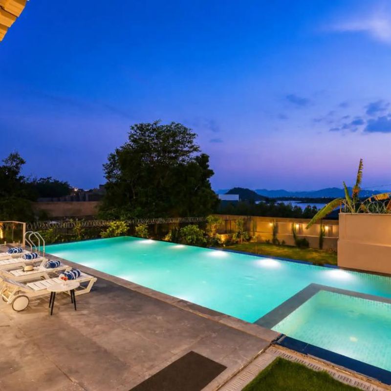 Illuminated swimming pool overlooking distant hills at twilight from a 9 BHK villa Udaipur.