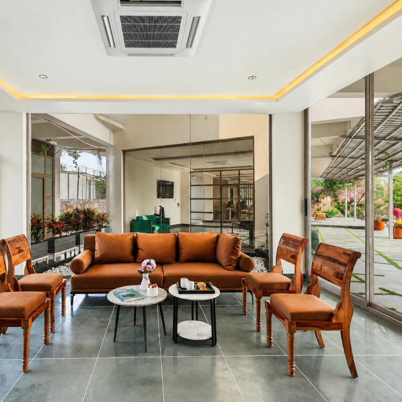 Large indoor living area with a brown sofa and wooden chairs at a large group villa with pool Udaipur.